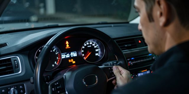 Tableau de bord d’une voiture éclairé, le voyant d’injection reste allumé tandis qu’un conducteur masculin attentif observe les instruments dans une ambiance réaliste et rassurante.