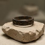 Quelles analyses choisir pour les bijoux en fer météoritique de Grèce antique ? Bague antique grecque en fer sombre présentée dans une vitrine de musée, avec des traces de corrosion visibles et un décor archéologique sobre.